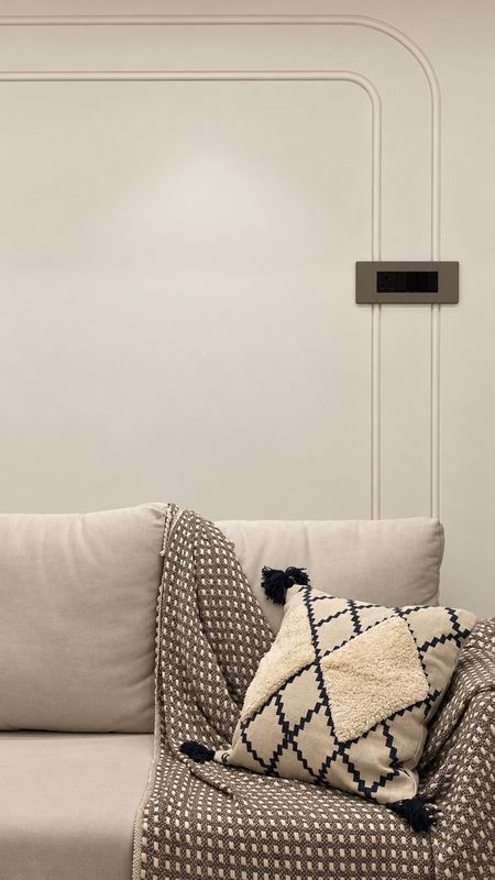 Linen sofa with a woven throw and a tasselled cushion against a cream wall with curved moulding