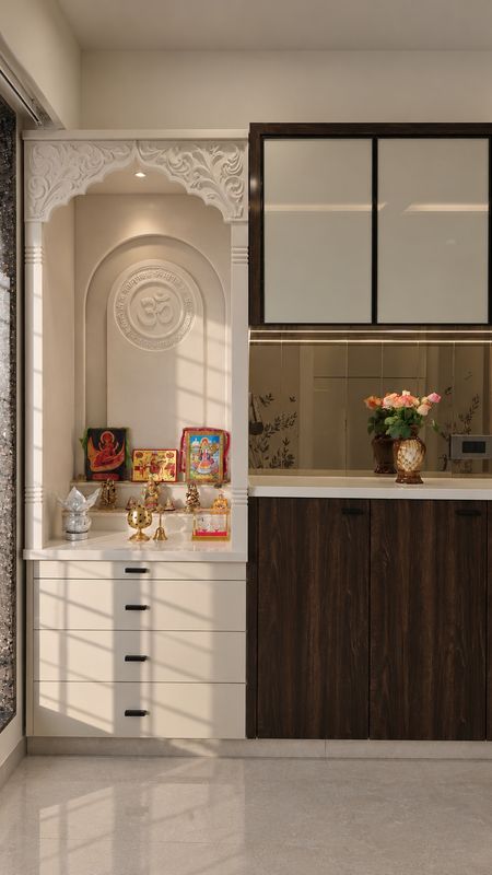 Mandir with a carved white arch and an Om panel beside a walnut crockery unit with a bronze mirror back, in afternoon sun