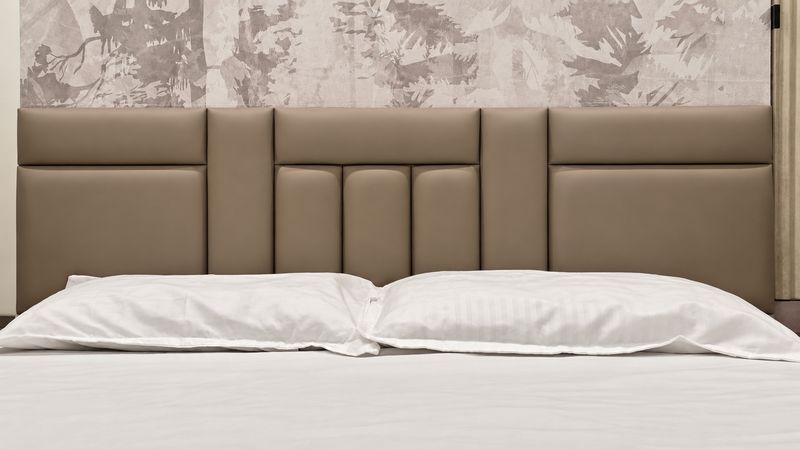 Close-up of a taupe leather-look panelled headboard under a soft forest-print wall