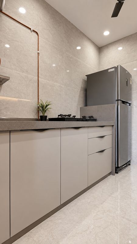Kitchen with matte cream cabinets, a grey quartz counter, a hob and a steel fridge against marble-look tiles