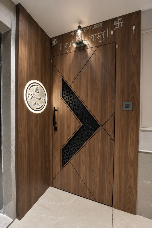 Entrance door in warm wood with a black geometric panel, a lit nameplate and a small lamp above