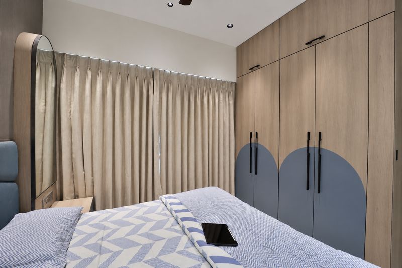 Wooden wardrobe with arched blue panels beside cream curtains