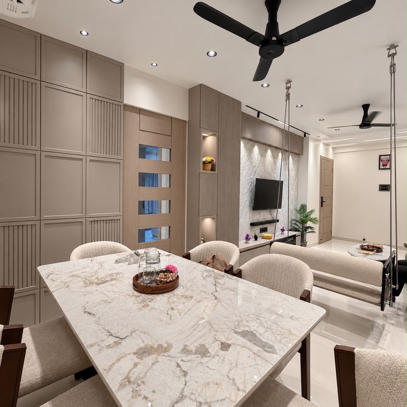 Dining area with a marble-top table, cream chairs, fluted taupe cabinets and a swing, with the living room beyond