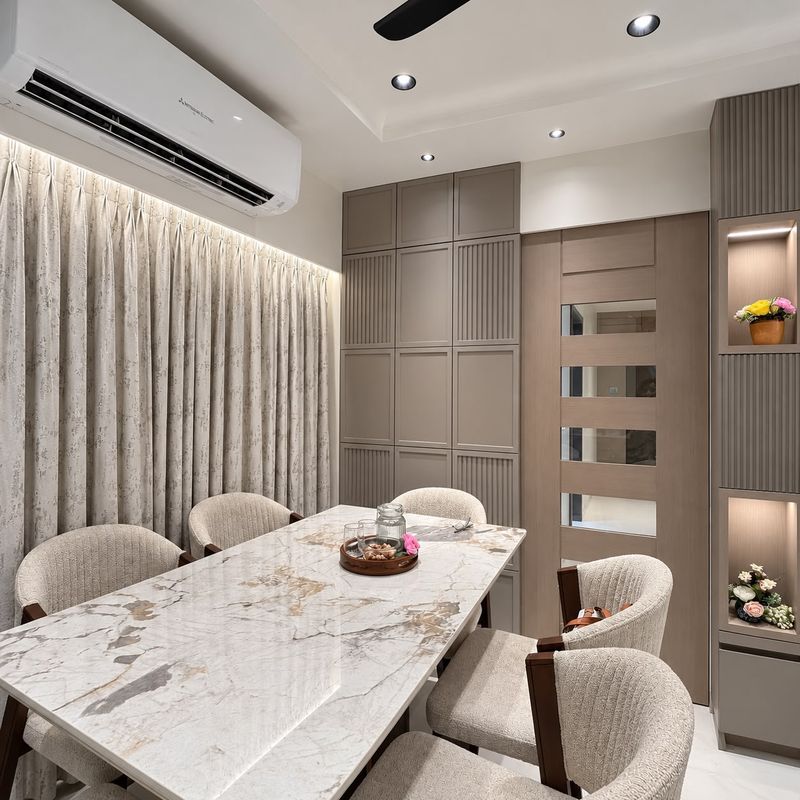 Dining corner with a marble table, pleated curtains lit from above, fluted cabinets and lit display niches