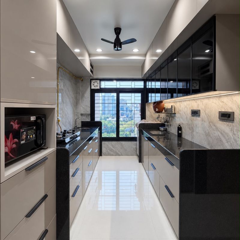 Galley kitchen towards a window, with taupe cabinets, black granite counters and a microwave in a tall unit
