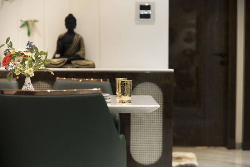 Dining area detail with green chairs, a cane panel and a brass Buddha