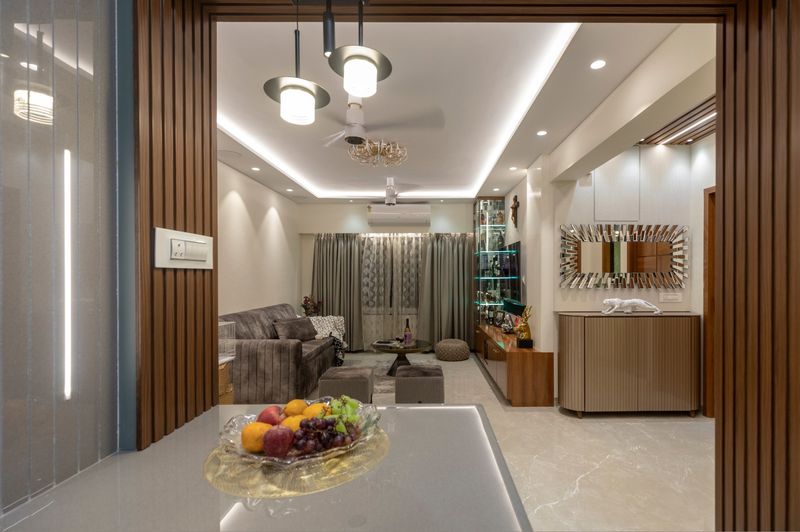 View from the kitchen counter through a fluted wood frame into the living room, with pendant lights and a cove ceiling