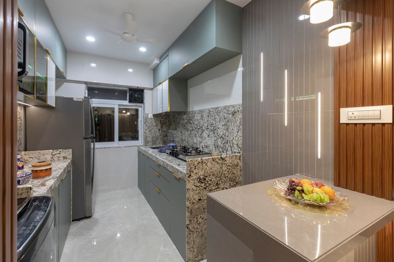 Galley kitchen with sage cabinets and granite, beside a breakfast counter lit by pendant lights and LED strips
