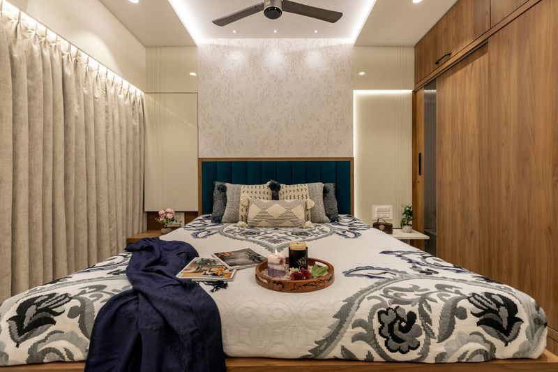 Bedroom with a teal padded headboard, floral wallpaper, linen curtains and a walnut sliding wardrobe
