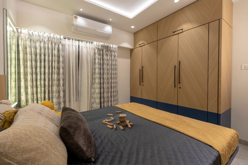 Kids' room with a chevron wood wardrobe on a blue base, printed curtains and a mustard throw on the bed