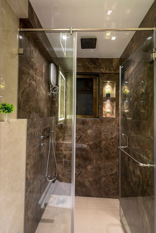 Glass-walled shower in dark brown marble-look tiles with a rain shower and lit niches with flowers